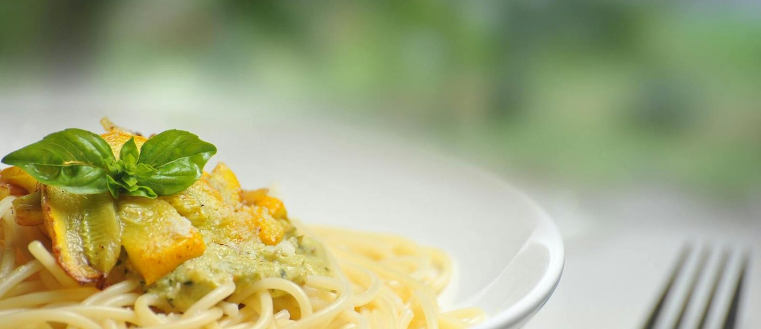 Close-up of freshly made spaghetti topped with basil and creamy pesto sauce in a white dish.