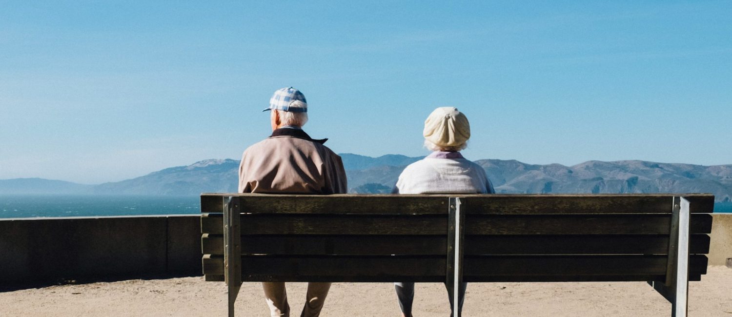 man and woman sitting on bench facing sea